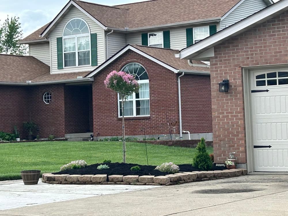 Front yard landscaping with a blooming tree, flower beds, and a brick house.