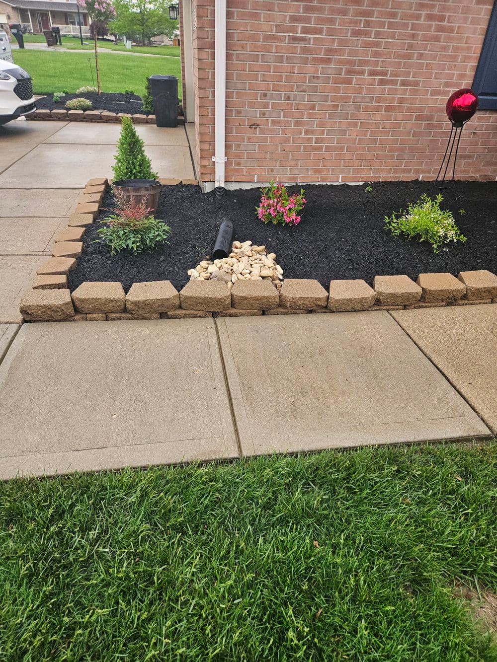 Landscaped garden with flower beds, decorative stones, and a drainage pipe by a brick home.