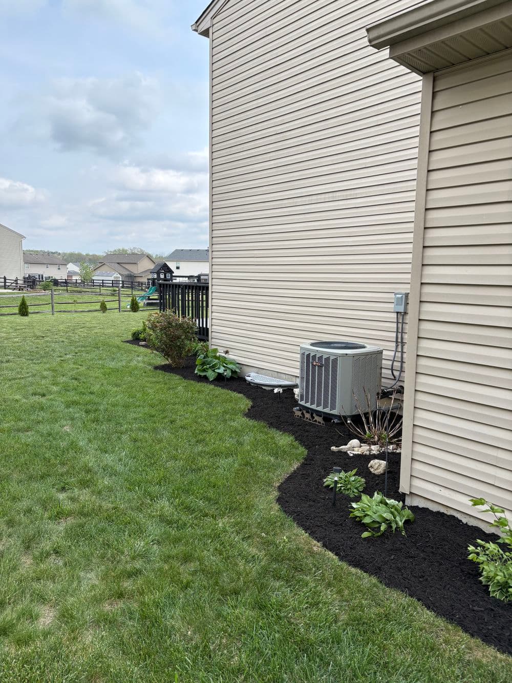 Well-maintained garden with grass and mulch beside a house and air conditioning unit.