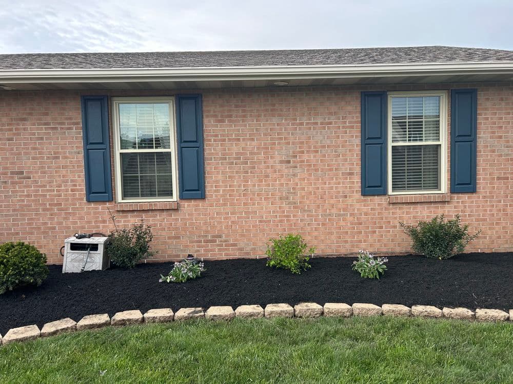 Brick home exterior with blue shutters, landscaped garden, and black mulch border.