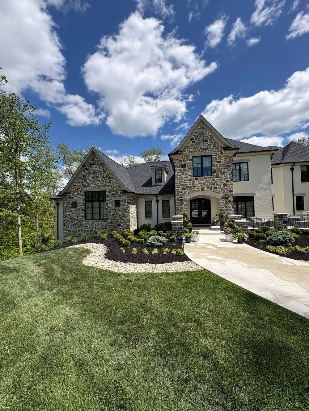 Elegant stone mansion with landscaped yard under a clear blue sky.