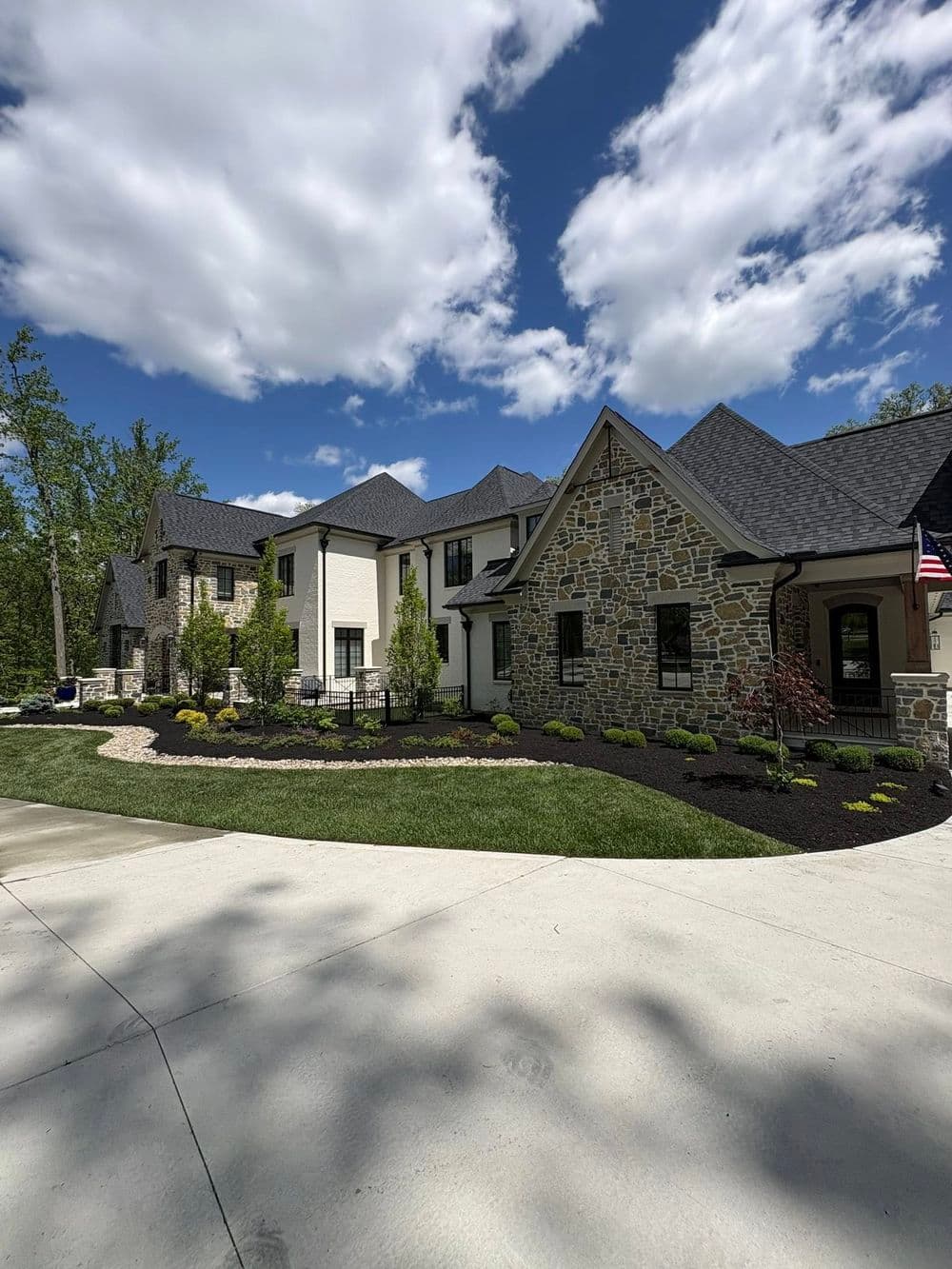 Modern stone and siding house with landscaped garden and blue sky backdrop.