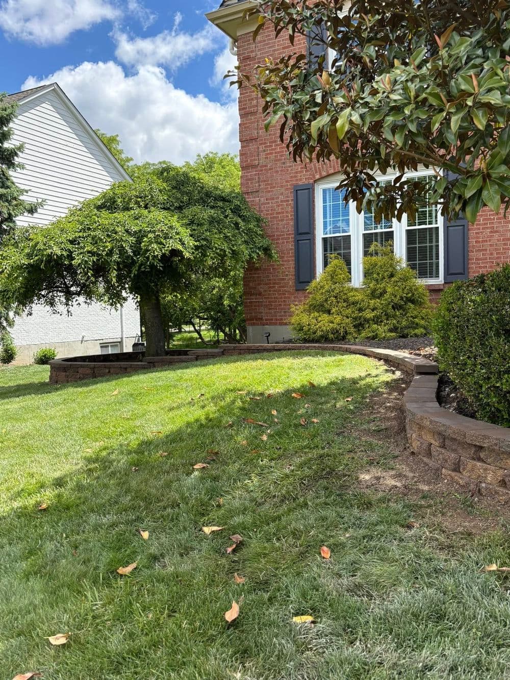 Landscaped yard featuring curved brick wall, lush greenery, and a red brick house.