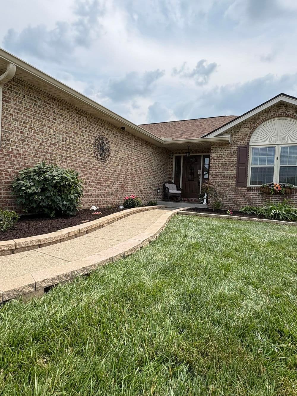 Charming brick home with landscaped front yard and winding pathway under cloudy sky.