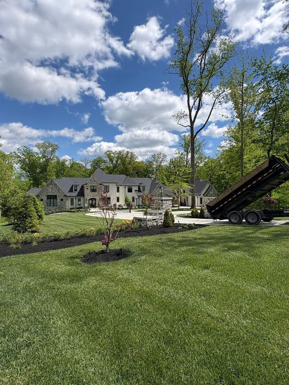 Luxury home with landscaped yard, trees, and a dump truck for construction work.