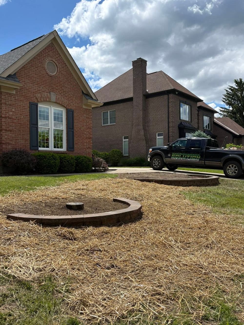 House landscaping with circular stone beds and a truck parked nearby on a sunny day.